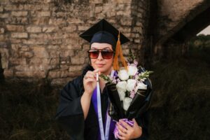 Graduation photo of woman in cap and gown standing in desert at golden hour in Southeast New Mexico