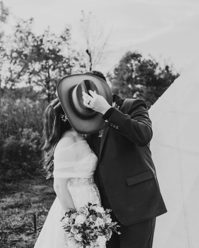 Bride and groom hiding behind cowboy hat